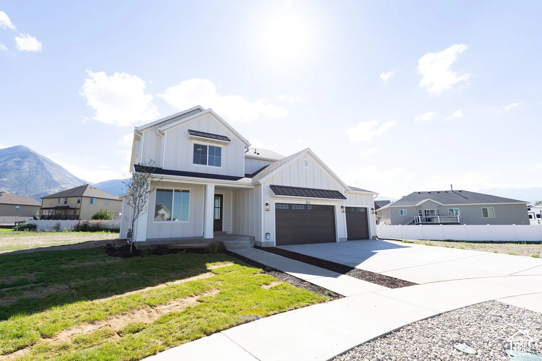 Two-story exterior featuring white board and batten siding, metal roof accents, an attached three-car garage, and a concrete driveway