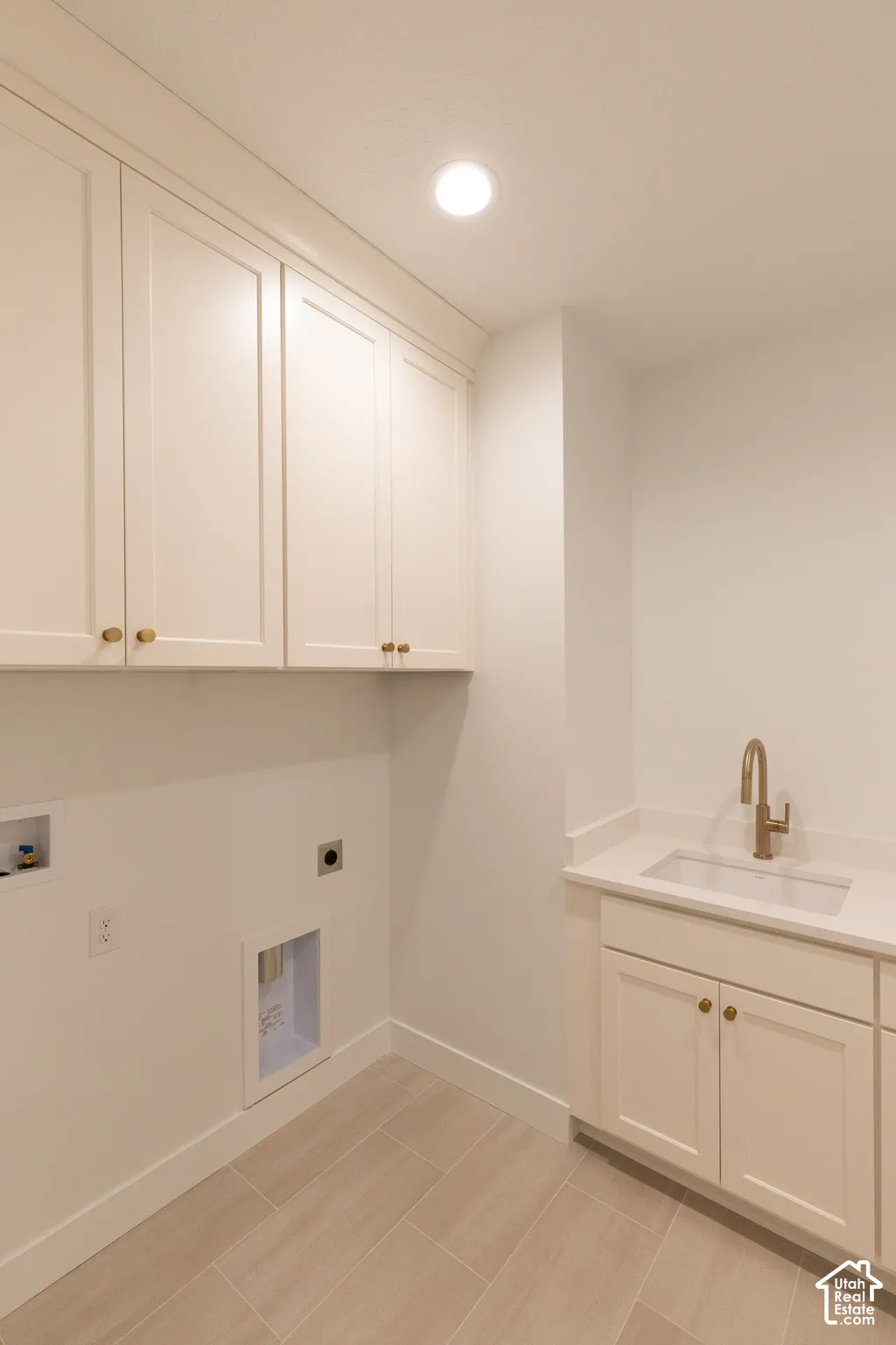 Laundry room featuring white Shaker-style cabinetry, a drop-in sink with a high-arch faucet, a stone-composite countertop, and wood-finish tile flooring