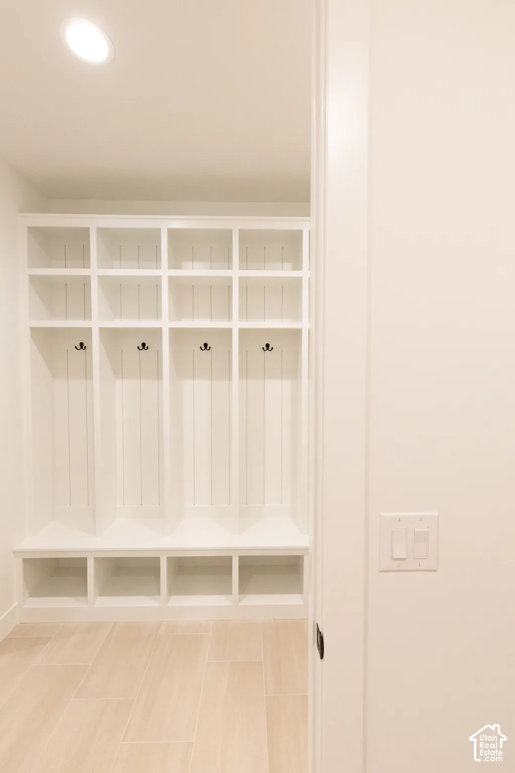 Built-in white cabinetry featuring vertical shiplap detailing, open cubby storage, and matte black hardware, finished with wood-finish flooring and recessed ceiling lighting