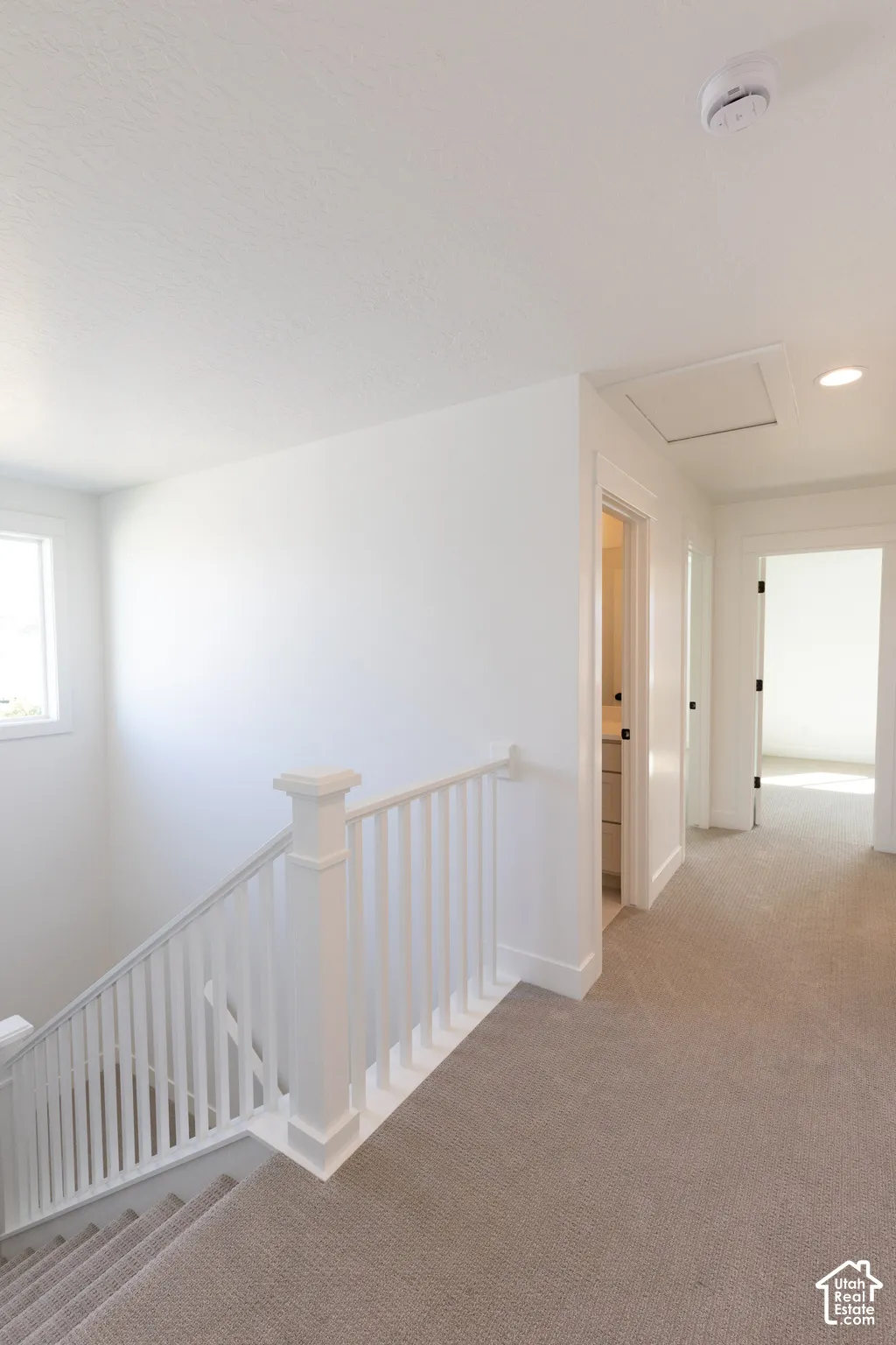 White staircase railing with square newel posts, wall-to-wall carpeting, and recessed lighting