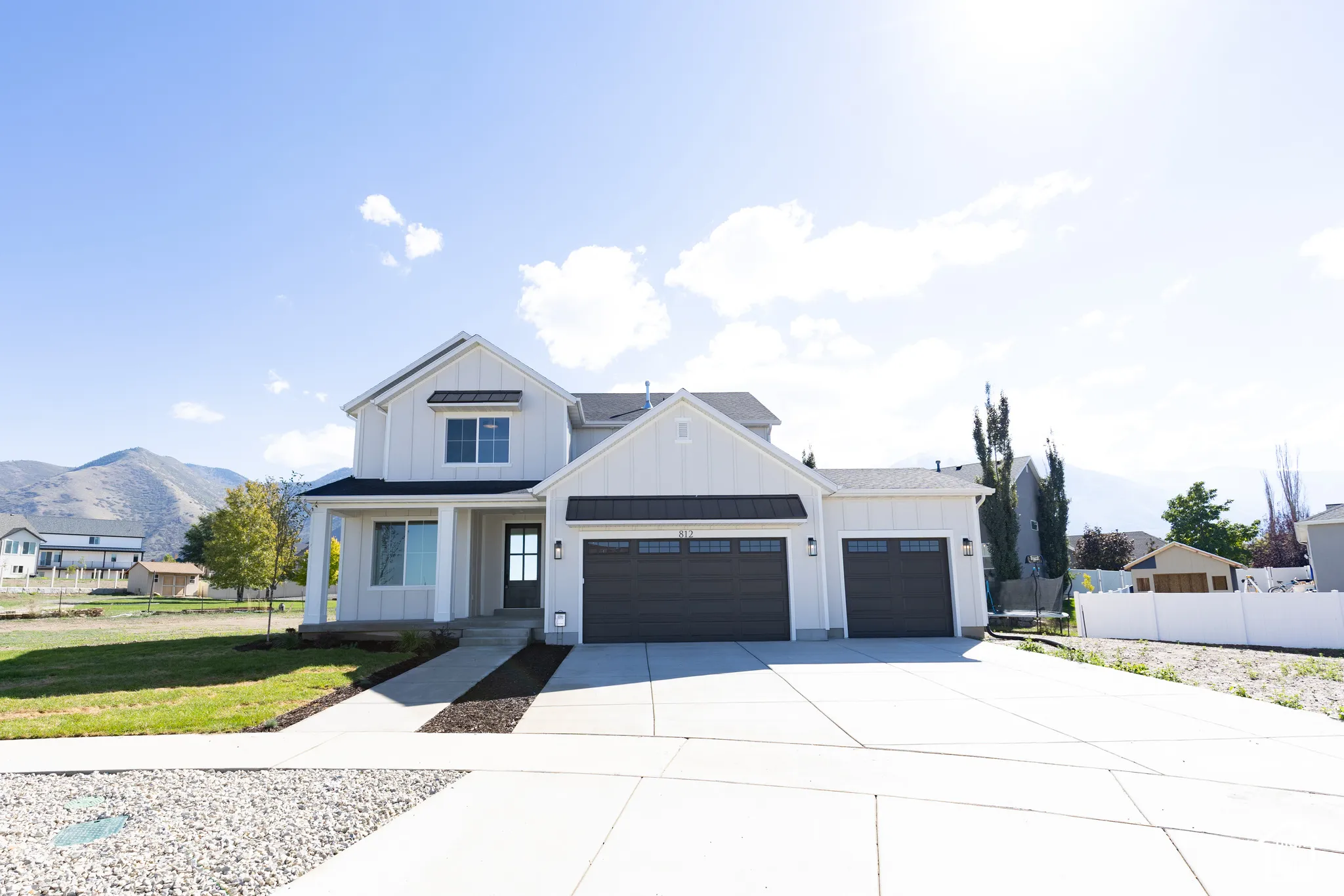 Two-story exterior featuring white vertical siding, a three-car garage with dark metal accents, a concrete driveway, and a mountain backdrop