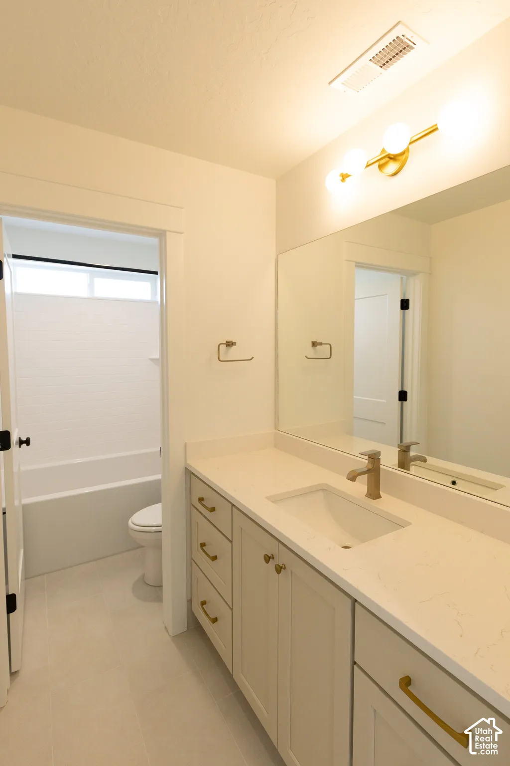 Bathroom vanity featuring a light-toned cabinet, stone-surface countertop with an integrated basin, brushed gold hardware, large frameless mirror, and modern globe lighting