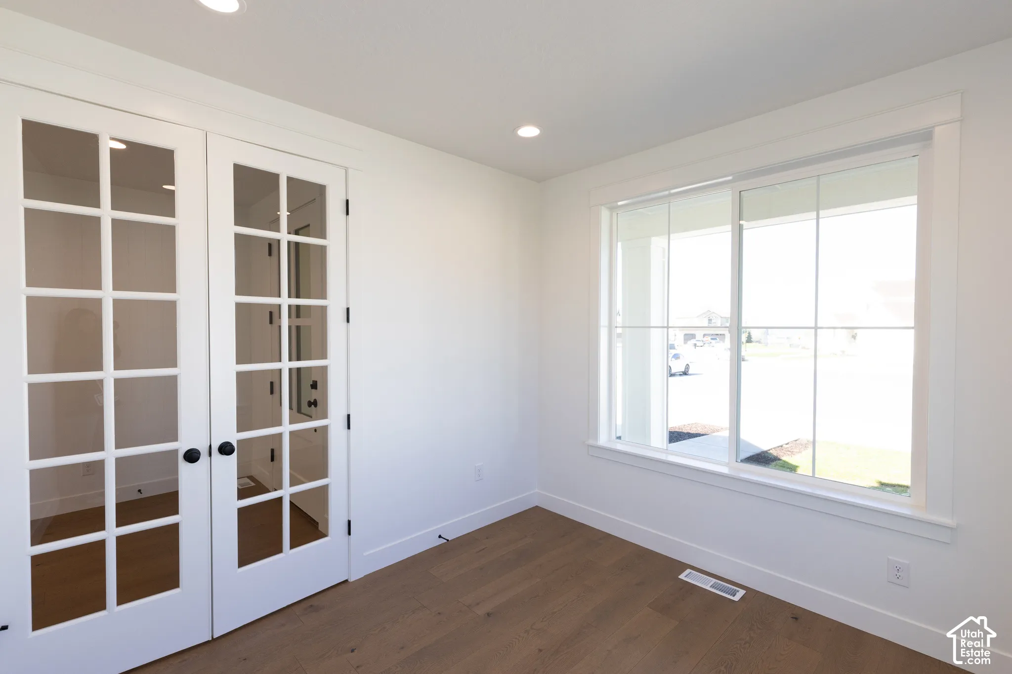Room featuring wood-finish flooring, white French doors with glass panes, and a large multi-pane sliding window with casing