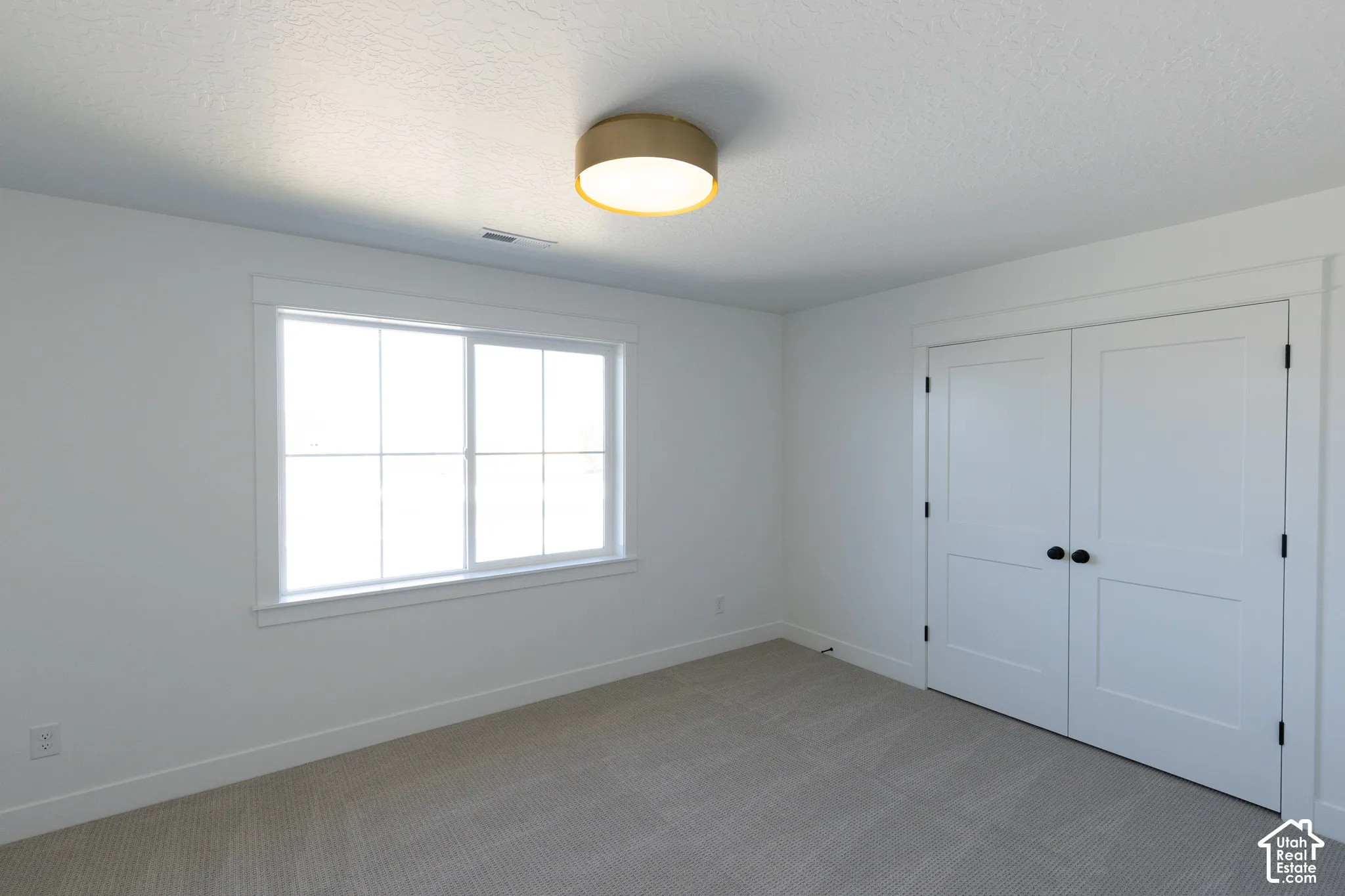 Neutral-toned carpeting, dual-panel closet doors with matte black hardware, multi-pane window with substantial trim, and a gold-tone flush-mount ceiling light fixture
