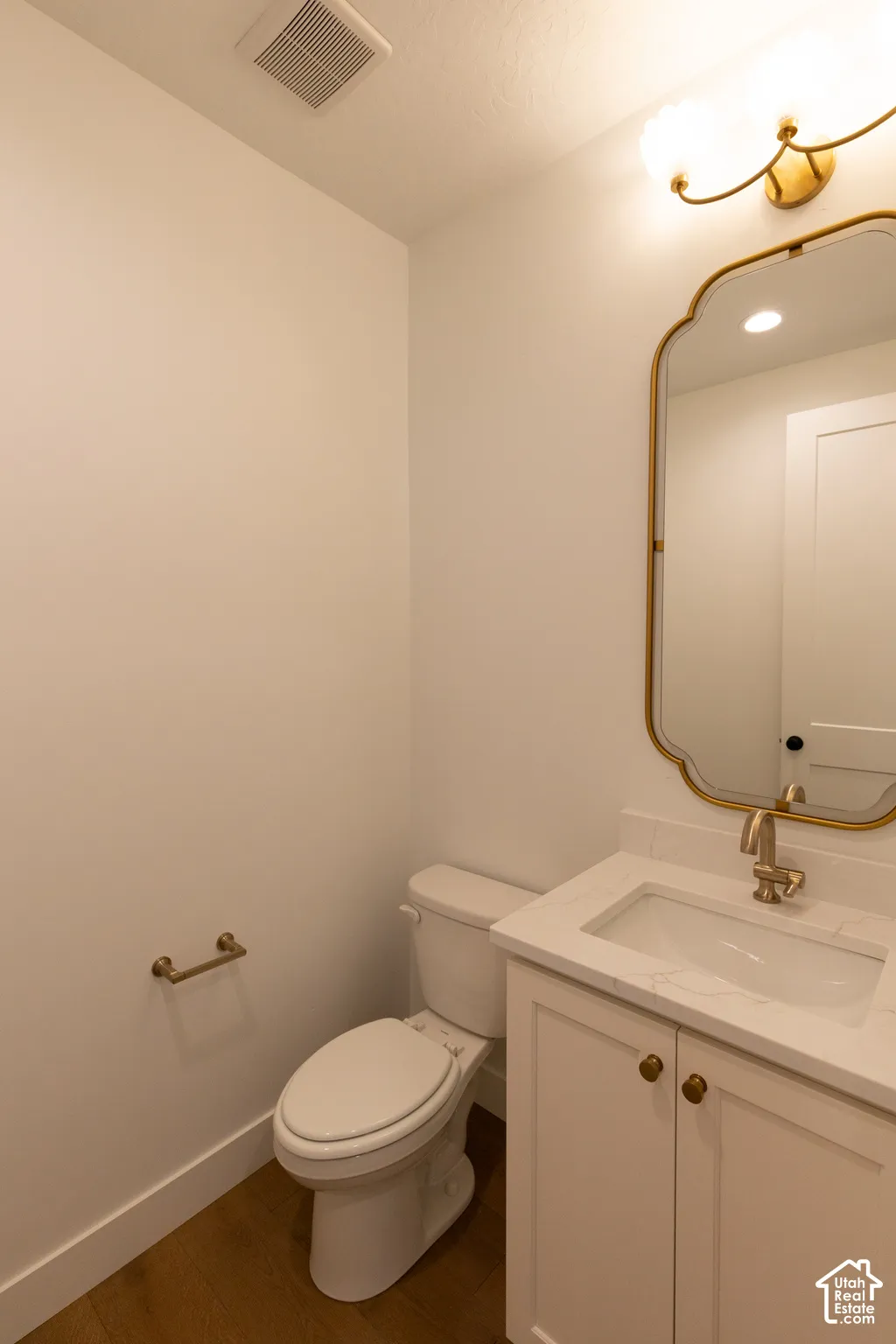 Bathroom featuring a stone-surface vanity with an integrated sink, gold-tone faucet, arched wall-mounted mirror, and wood-finish flooring