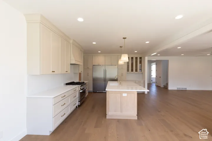 Kitchen featuring custom cabinetry, quartz countertops, a central island with wood-finish base, stainless steel appliances, and wood-finish flooring