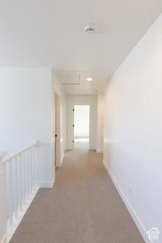 Hallway featuring neutral-toned carpeting, white walls, a white wooden balustrade, recessed ceiling lighting, and an attic access panel