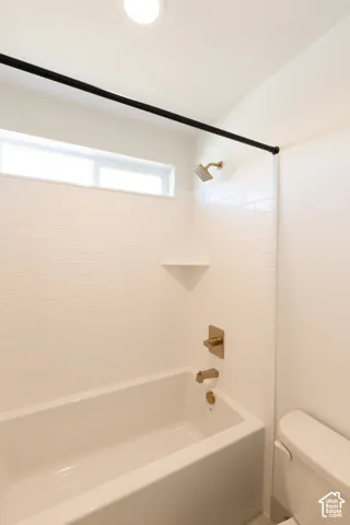 Bathtub and shower surround featuring white subway tile, a built-in corner shelf, rectangular matte metallic hardware, and a horizontal transom window