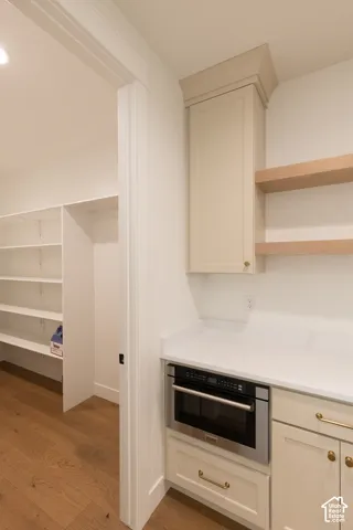 Custom cabinetry with brass-tone hardware, white stone-finish countertops, built-in microwave, light wood floating shelves, and wood-finish flooring