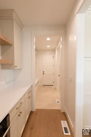 Custom cabinetry with gold-tone hardware, white stone-finish countertops, open wood shelving, wood-finish flooring, and recessed ceiling lighting