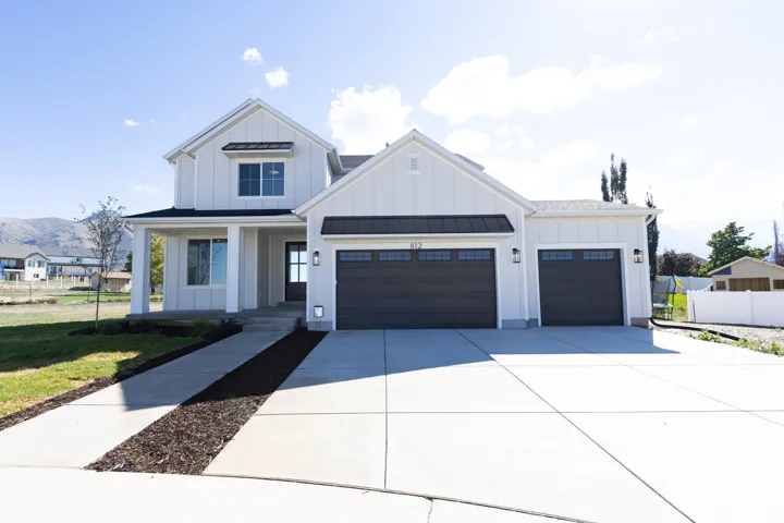 Two-story modern farmhouse exterior featuring vertical siding, metal roof accents, a three-car garage, and a concrete driveway