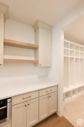 Custom cabinetry with light-toned finish, quartz countertops, floating wood-finish shelving, and integrated white built-in storage lockers