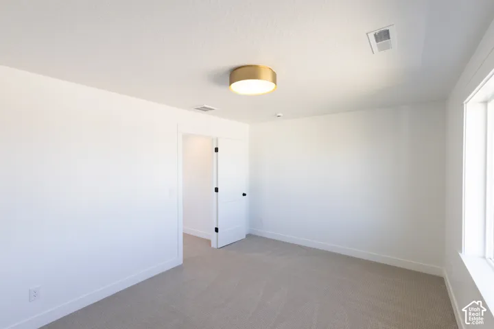 Neutral interior room featuring neutral carpeting, a brushed-gold finish flush-mount light fixture, and a white two-panel interior door with matte black hardware