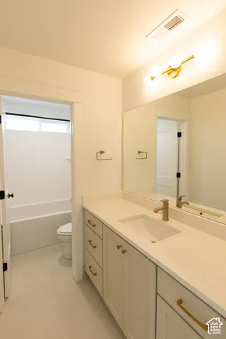 Bathroom vanity featuring a light-toned cabinet, stone-surface countertop with an integrated basin, brushed gold hardware, large frameless mirror, and modern globe lighting