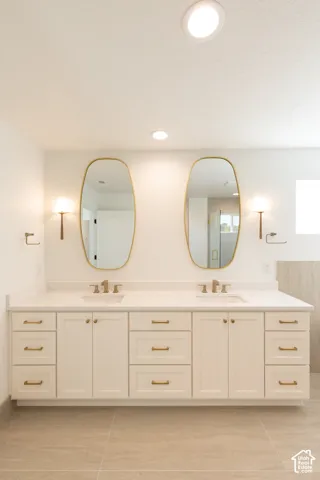 Double vanity featuring a light-toned cabinet finish, quartz countertop with dual integrated sinks, gold-tone hardware, oval mirrors, and wall-mounted light fixtures