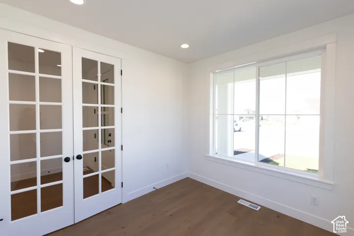 Room featuring wood-finish flooring, white French doors with glass panes, and a large multi-pane sliding window with casing