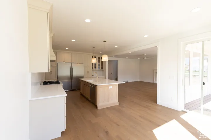 Kitchen featuring light-toned wood-finish flooring, a central island with a stone-finish countertop, stainless steel appliances, recessed ceiling lighting, and glass-paned sliding doors