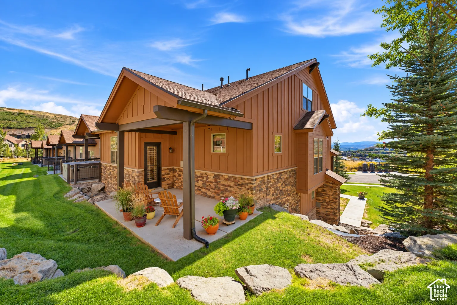 Exterior featuring vertical wood-finish siding, stone masonry accents, a covered concrete patio, and a shingled roofline
