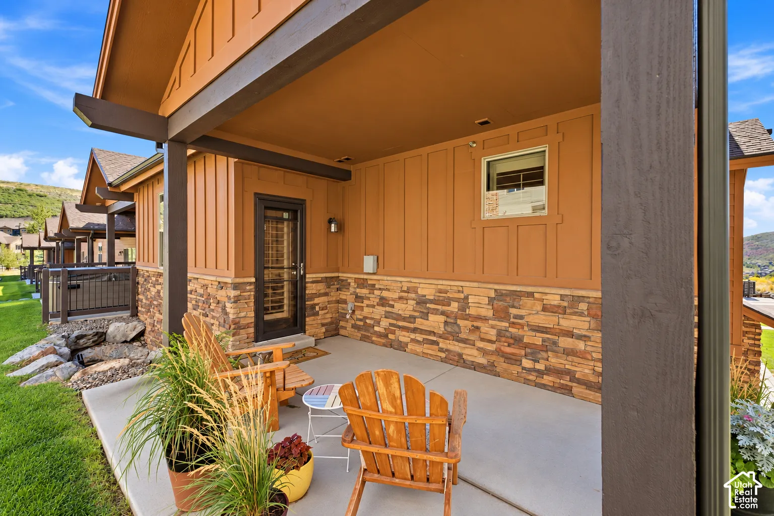 Covered patio featuring vertical board-and-batten siding, stone veneer wainscoting, and exposed timber beams