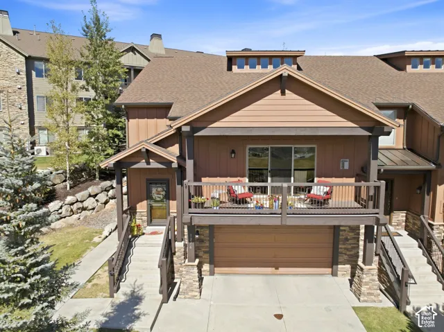 Multi-level exterior featuring horizontal and vertical siding, stone masonry accents, a private second-story balcony, and an attached garage
