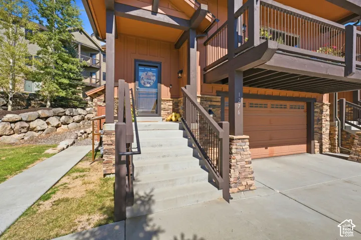 Multi-level exterior featuring stone veneer accents, wood-finish siding, a private balcony with metal railings, a concrete stairway, and an attached garage