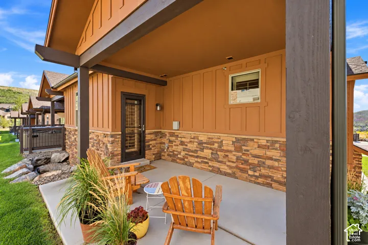 Covered patio featuring vertical board-and-batten siding, stone veneer wainscoting, and exposed timber beams