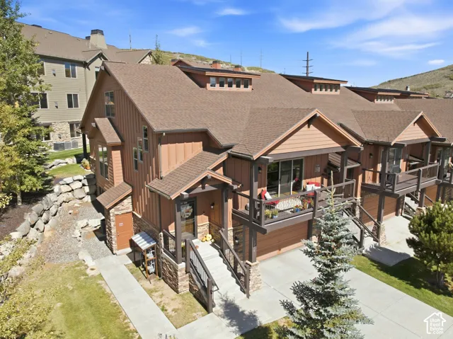 Multi-level exterior featuring vertical board-and-batten siding, stone masonry accents, a tiered shingle roofline, private covered balconies with railings, and a concrete driveway
