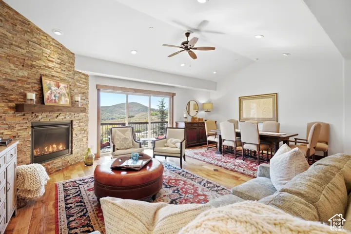 Vaulted ceilings featuring recessed lighting and a central ceiling fan, floor-to-ceiling stone-ledger fireplace with a timber mantel, wood-finish flooring, and sliding glass doors revealing mountain scenery