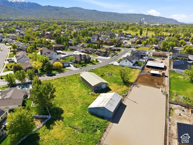 Aerial perspective of a multi-acre property featuring two detached outbuildings, a fenced riding arena, extensive pasture area, and mountain backdrop