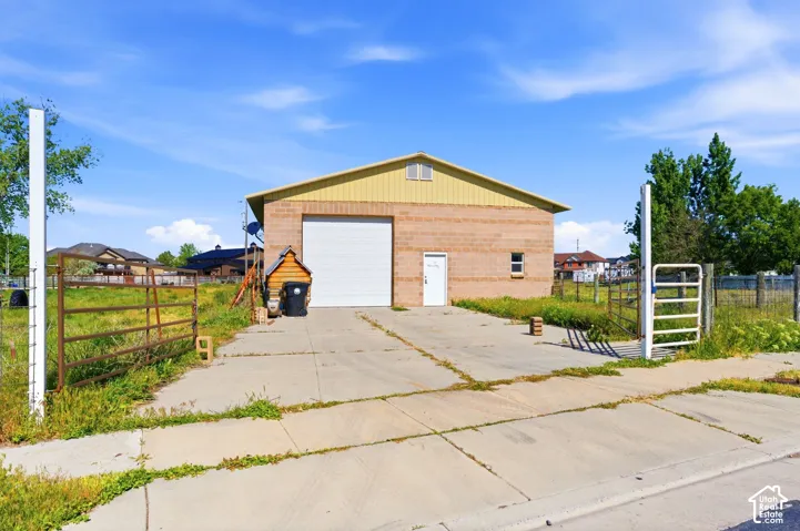Detached workshop featuring masonry exterior construction, metal roofing, a large overhead garage door, a pedestrian entry door, and concrete driveway access