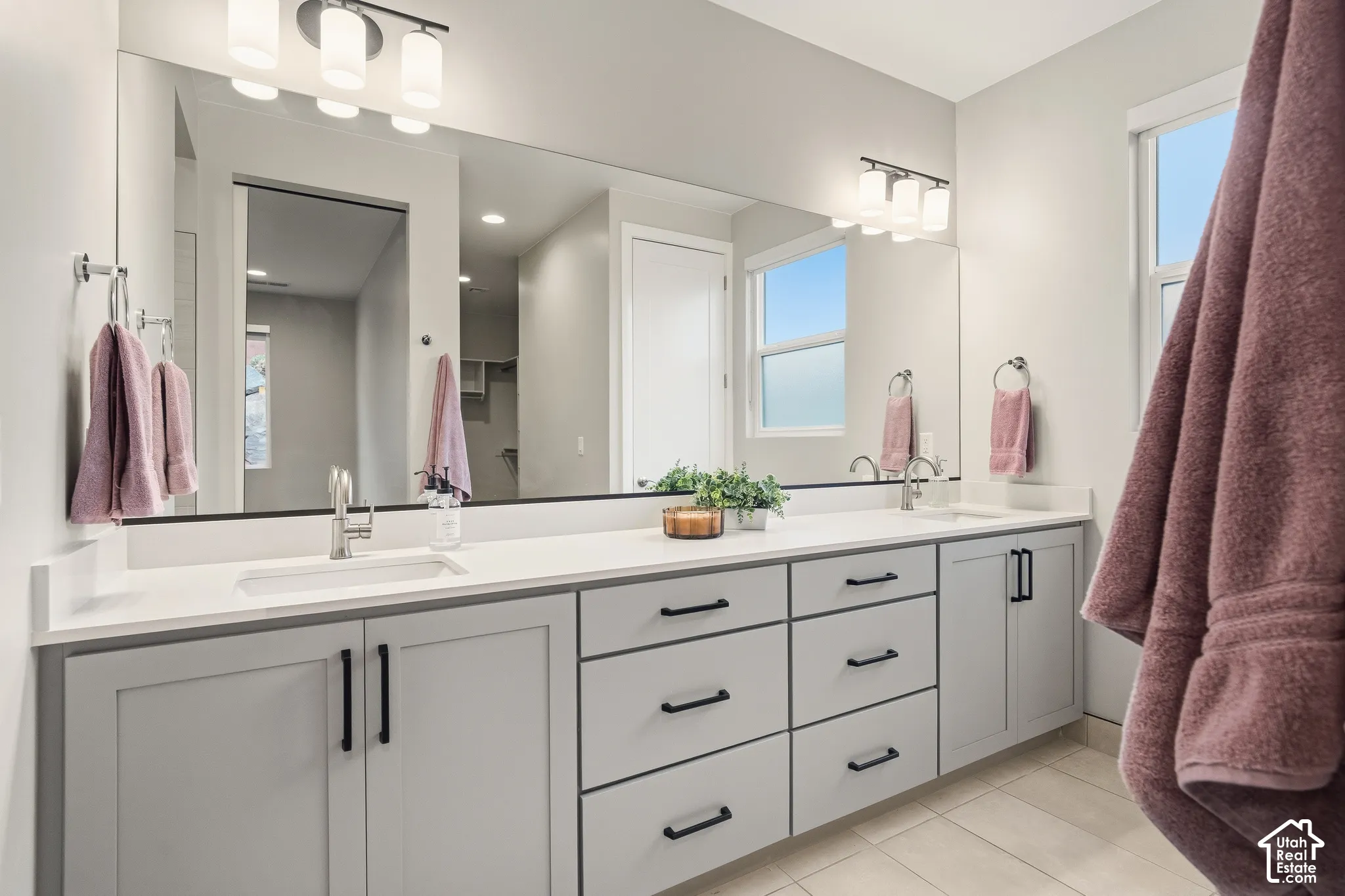 Dual-sink vanity with light-gray cabinetry, solid-surface countertop, matte black hardware, and an expansive wall-to-wall mirror