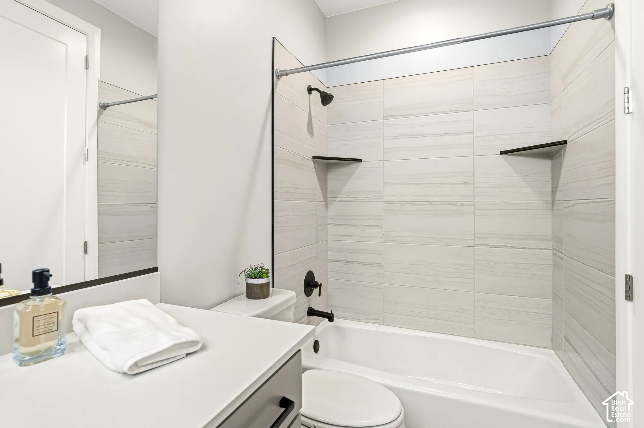 Bathroom featuring a vanity with a white countertop, bathtub with horizontal tile surround, integrated shelving, and matte black hardware