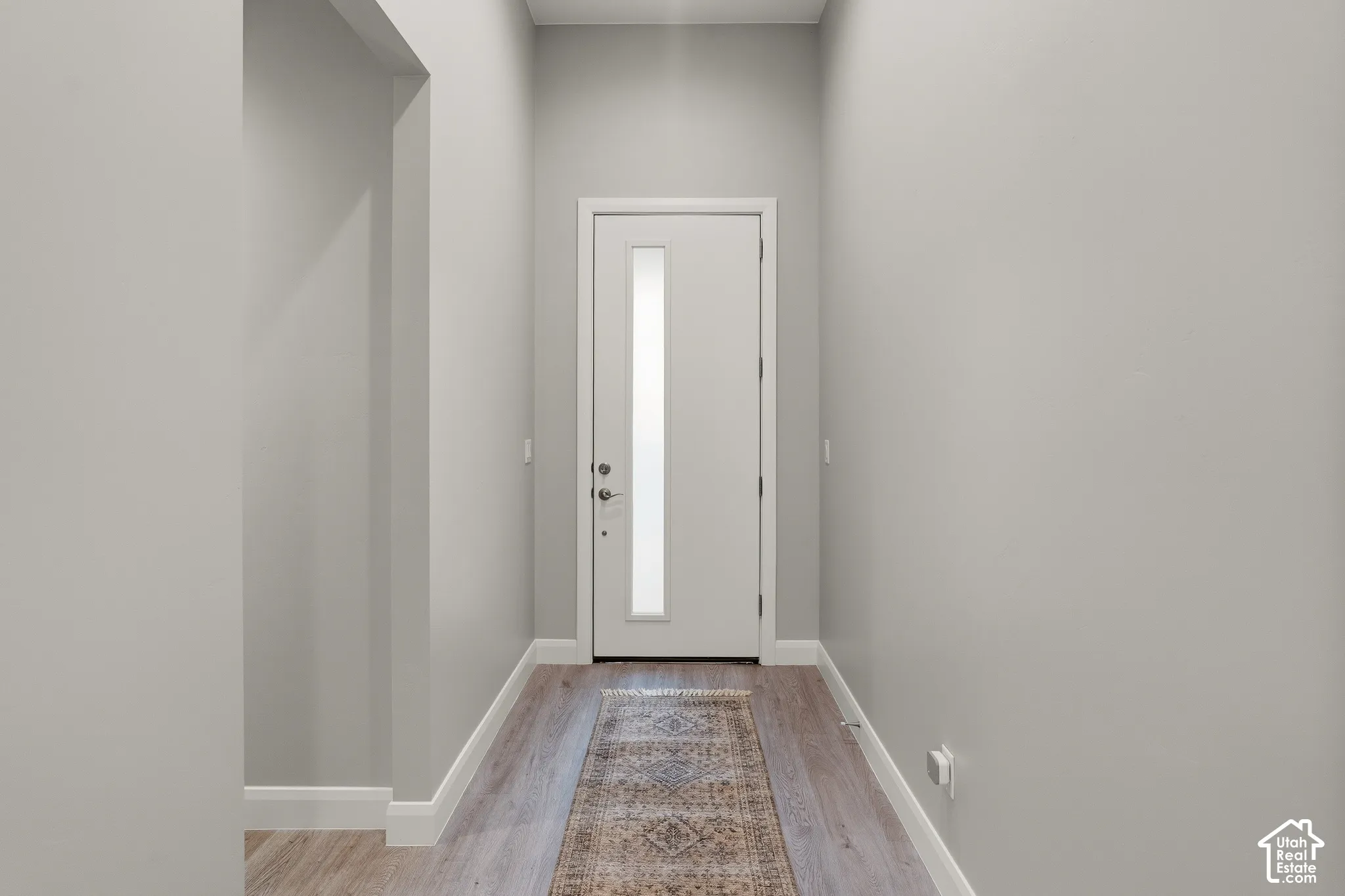 Entryway featuring wood-finish flooring, high ceilings, and an exterior door with a vertical frosted glass inset and brushed metal hardware
