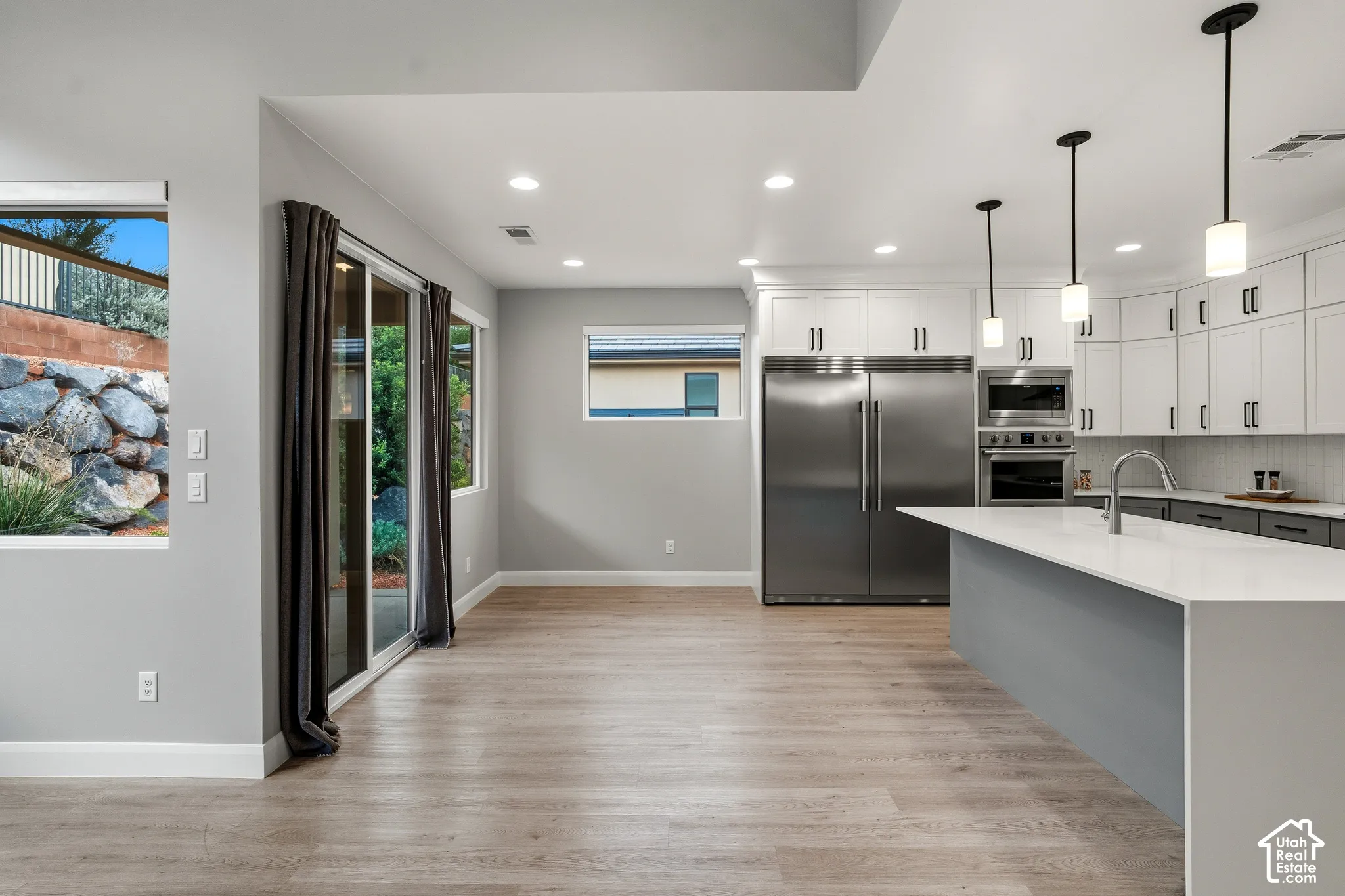Kitchen featuring white upper cabinetry, stainless steel appliances, a center island with a solid-surface countertop, recessed lighting, and wood-finish flooring