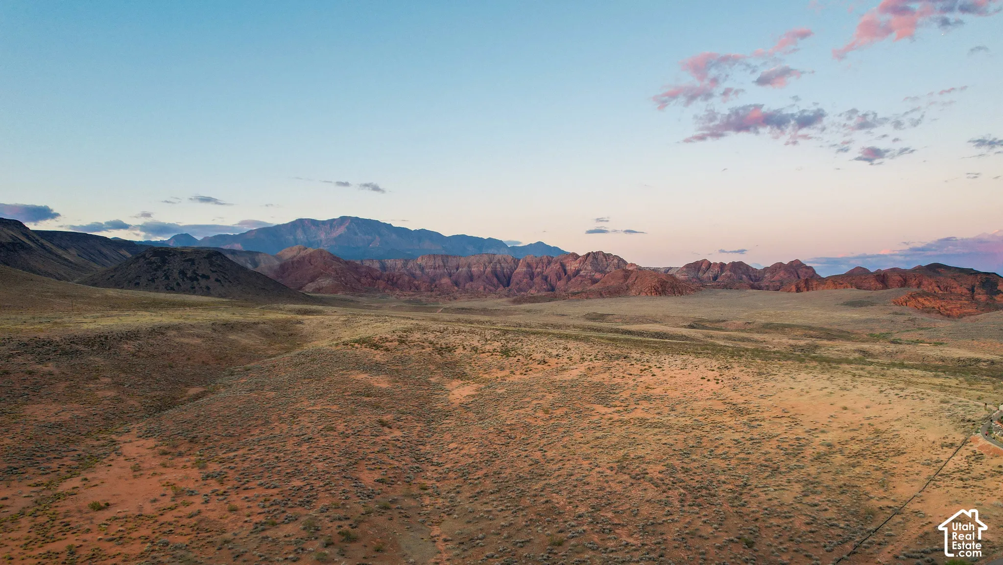 Expansive desert landscape featuring rolling terrain, rock formations, and mountain backdrop