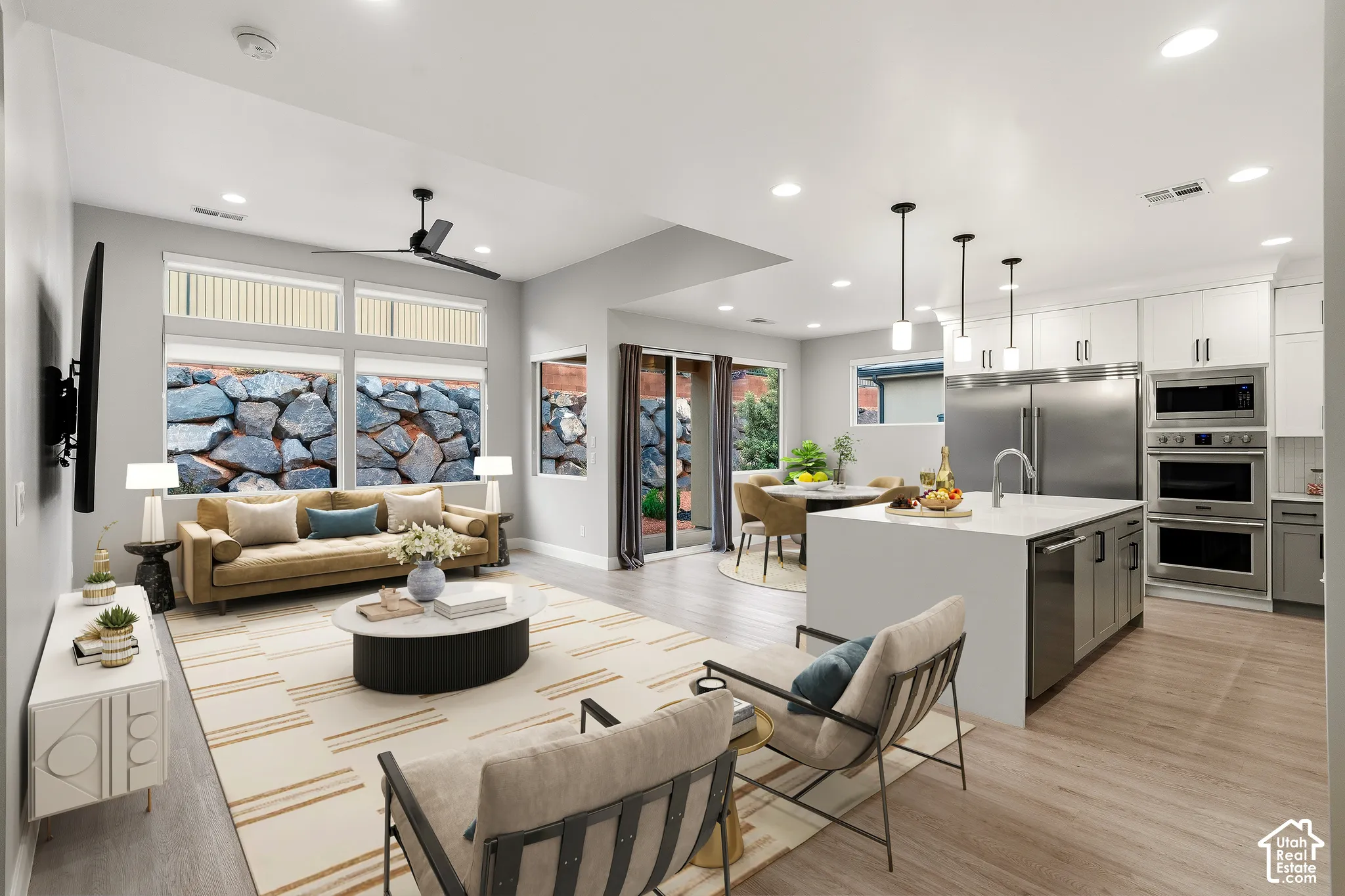 Open-concept layout featuring wood-finish flooring, recessed lighting, stainless steel appliances, a center island with countertop seating, and stacked-stone exterior wall elements