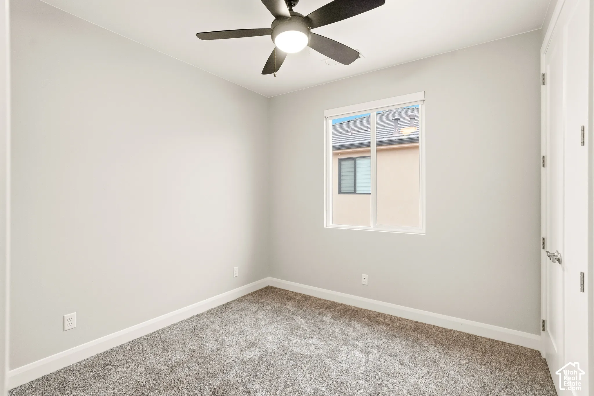 Neutral-toned interior space featuring wall-to-wall carpeting, a multi-blade ceiling fan with integrated lighting, and a dual-pane sliding window