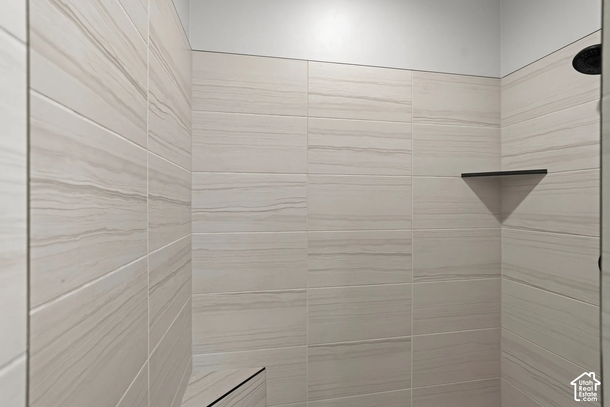 Shower featuring floor-to-ceiling horizontal tile, built-in corner tile bench, integrated corner shelving, and matte black plumbing fixtures