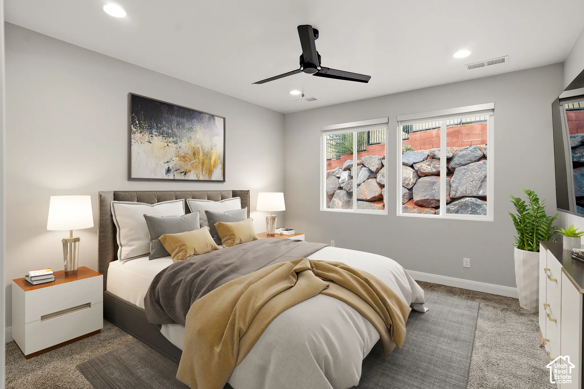Neutral-toned interior featuring carpeting, recessed lighting, a matte black ceiling fan, and dual-pane windows with integrated stone retaining wall scenery