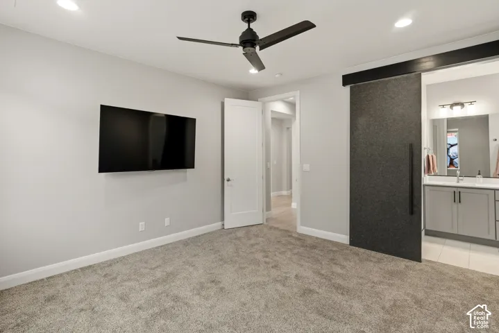 Room interior featuring neutral wall paint, charcoal-colored sliding barn door, recessed lighting, matte black ceiling fan, and grey cabinetry with a rectangular mirror