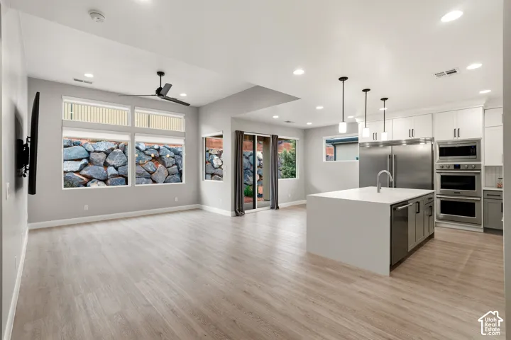 Open-concept interior featuring light wood-finish flooring, a center island with solid surface countertop, stainless steel double wall ovens, recessed lighting, and large windows with integrated rock wall exterior elements