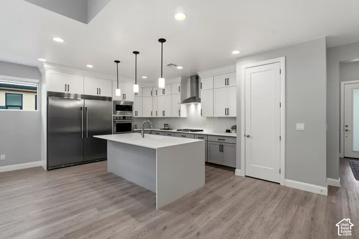 Kitchen featuring wood-finish flooring, quartz-topped center island with sink, stainless steel appliances, floor-to-ceiling white cabinetry, and pendant lighting
