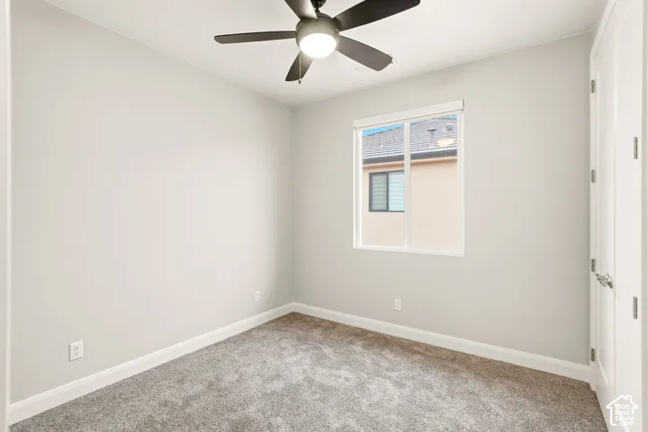 Neutral-toned interior space featuring wall-to-wall carpeting, a multi-blade ceiling fan with integrated lighting, and a dual-pane sliding window