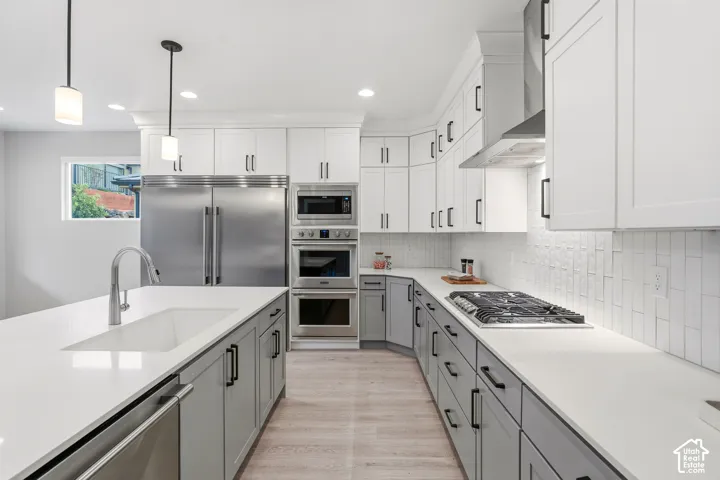 Kitchen featuring shaker-style cabinetry, a central island with a farmhouse sink, stainless steel built-in appliances, quartz countertops, and white vertical subway tile backsplash