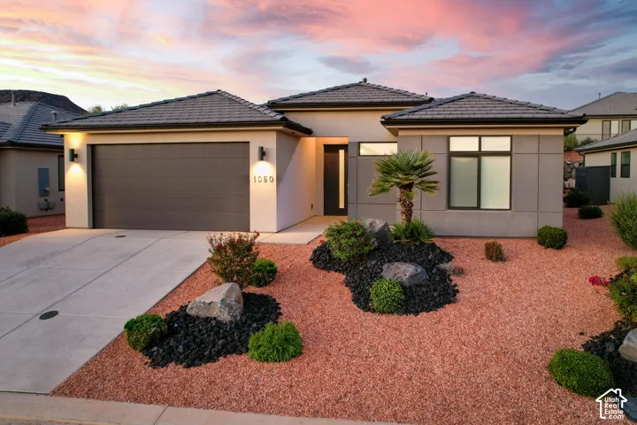 Modern exterior featuring a smooth stucco facade, concrete tile roof, attached two-car garage, and xeriscaped front yard with decorative rock and boulder accents