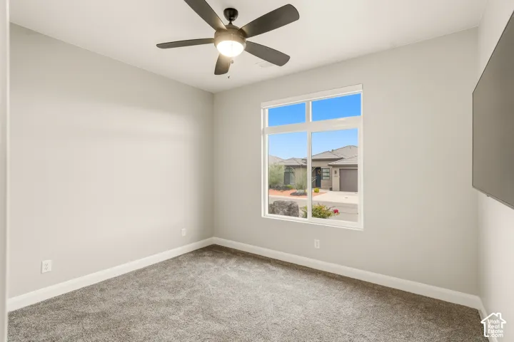 Neutral interior room featuring neutral-toned carpeting, a ceiling fan with integrated lighting, and a multi-pane window