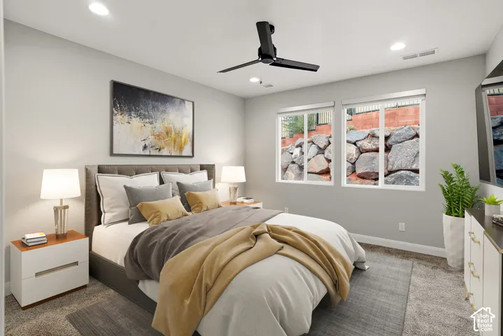 Neutral-toned interior featuring carpeting, recessed lighting, a matte black ceiling fan, and dual-pane windows with integrated stone retaining wall scenery
