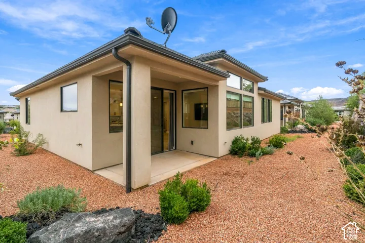 Stucco exterior featuring a covered patio, large rectangular windows, multi-pane transom windows, and low-maintenance rock landscaping