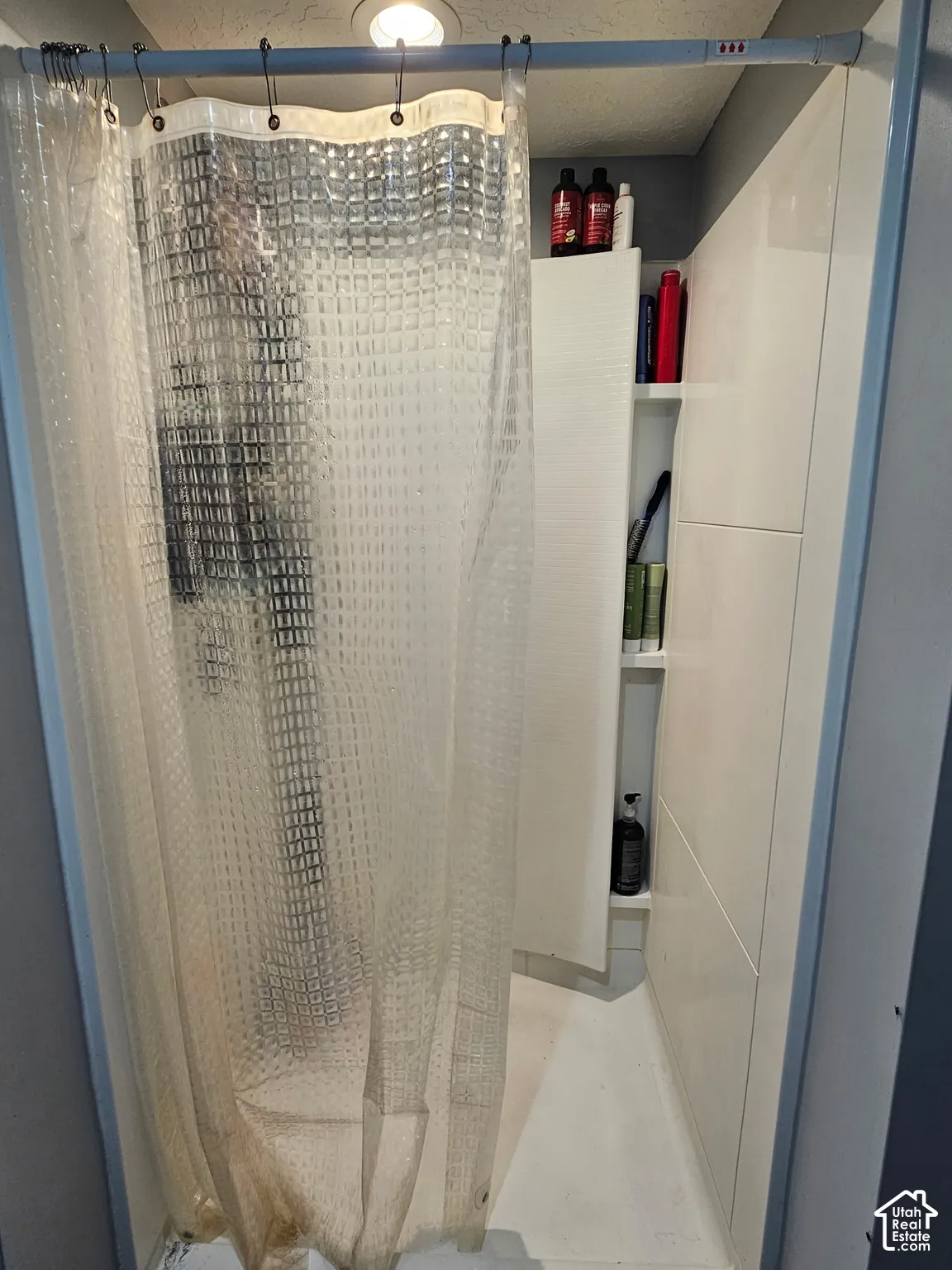 Shower stall featuring smooth white wall surrounds, integrated built-in shelving, and recessed ceiling lighting