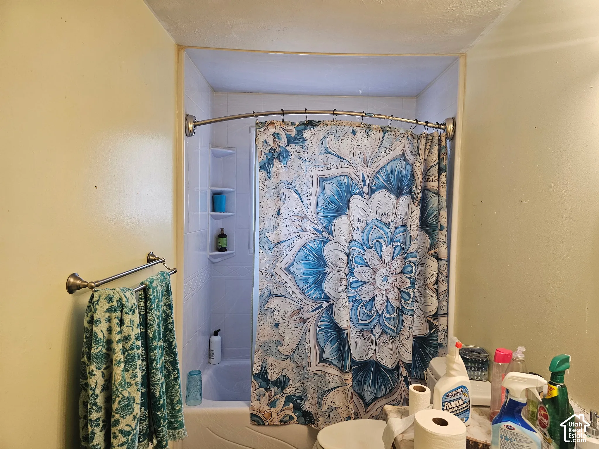 Shower alcove featuring white tile surround, integrated shelving, and a curved shower rod